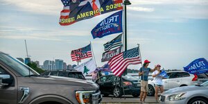 zig Trump-Flaggen wehen im Wind. Davor Pick-Up-Trucks. Trump-Unterstützer am Feiern.