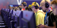 Eine Reihe von Jungs stehen bei der Spielemesse Gamescom mit Kopfhörern und Controllern vor Bildschirmen