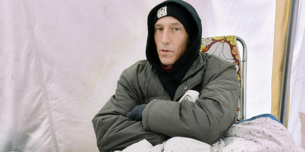 Hungerstreikender Klimaaktivist in viel Kleidung gehüllt stitzt auf einem Klappstuhl