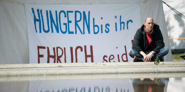 Wolfgang Metzeler-Kick. der sitzt im Schneidersitz vor einem Zelt, an dem ein Transparent angebracht ist: Hungern bis ihr ehrlich seid