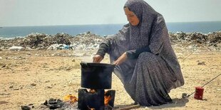 eine Frau am Strand rührt in einem Topf, der auf einem Feuer steht