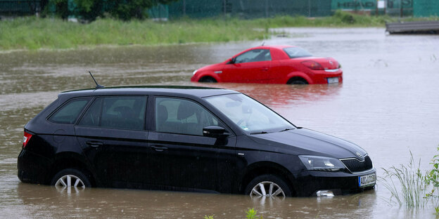 Zwei Autos stehen auf einem Parkplatz, halb unter Wasser