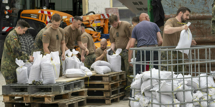 Bundeswehrsoldaten mit Sandsäcken, dahinter ein Bagger