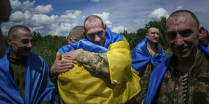 Zwei Männer umarmen sich. Einer davon ist in eine ukrainische Flagge gehüllt