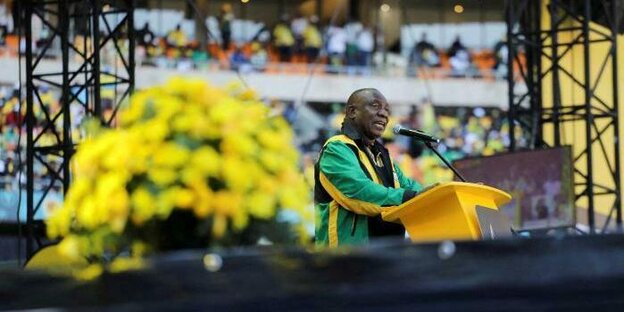 Cyril Ramphosa hält auf einem Podium eine Rede. Im Hintergrund sind Ränge eines Stadions zu erkennen