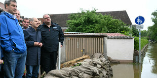 Söder und Scholz schauen an Sandsäcken auf Hochwasser.