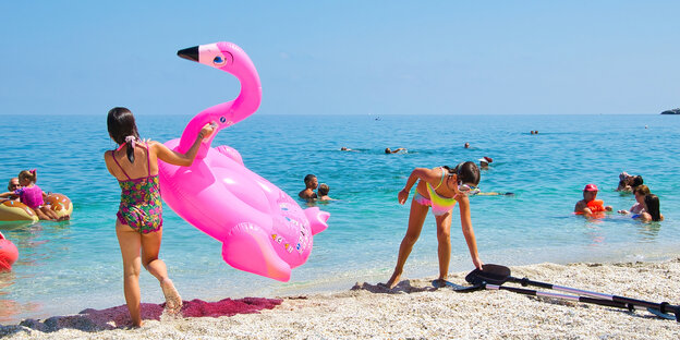 Kinder an einem Strand mit einem aufblasbaren Flamingo.