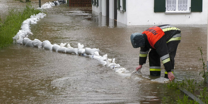 Feurwehrmann richtet Sandsäcke in einem überfluteten Gebiet aus.