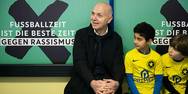 FB-Präsident Bernd Neuendorf (l) sitzt beim Start der Antirassismus-Kampagne des DFB mit zwei Nachwuchsfussballern.