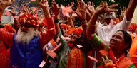 Bunt gekleidete Menschen freudig die Hände nach oben reckend, orange Papierschnipsel fliegen
