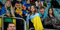 Fiusballfans in einem Stadion, eine Frau hat sich eine ukrainische Fahne über die Schultern gelegt