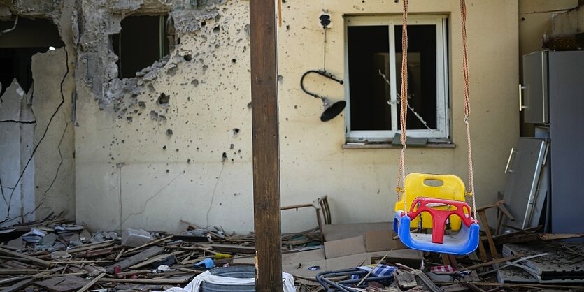 Eine Kinderschaukel vor einem zerstörten Haus