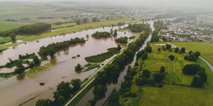 Luftaufnahme eines über die Ufer getretenen Flusses, die Ufer sind weitgehend grün, teilweise bebaut