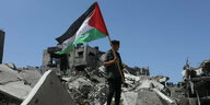 Ein Palästinenser hält die palästinensische Fahne in der Hand, während er in Chan Junis auf Trümmern nach israelischem Beschuss steht.