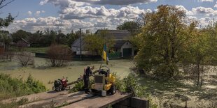 Ein Mann steht an einer Maschine, die Wasser aus einem überfluteten Dorf abpumpt, die ukrainische Flagge ist auf der Maschine