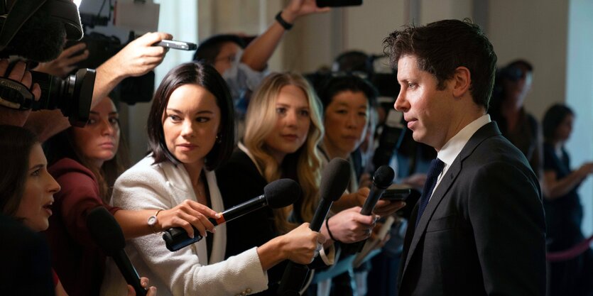 Eine Person vor Journalist:innen mit Mikrofonen.