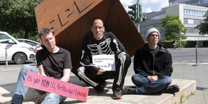 Drei Hungerstreiker mit Forderungen hocken vor einem rostigen SPD Würfel