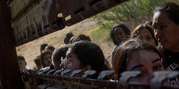 Frauen schauen durch einen Schlitz in einer verrosteten Stahlmauer