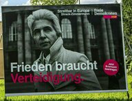 FDP-Wahlplakat: Porträt Strack-Zimmermanns mit hochgeschlagenem Mantelkragen vor dem Reichstag in Schwarz-Weiß und dem Slogan: Frieden braucht Verteidigung