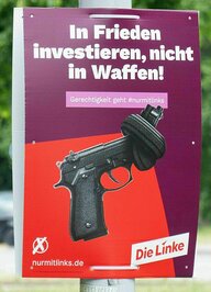 Plakat der Linken: Auf rotem Grund ist eine Pistole mit Knoten im Lauf zu sehen und der Slogan: Investiert in Frieden, nicht in Waffen