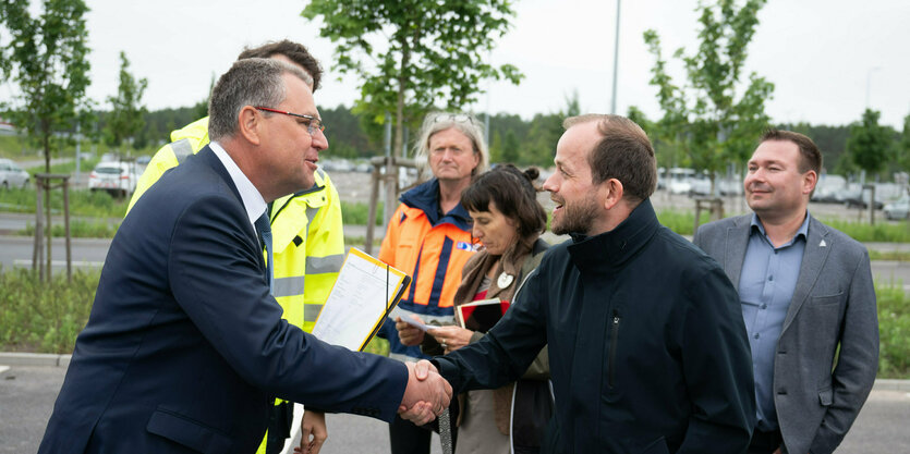 Minister für Infrastruktur und Landesplanung des Landes Brandenburg, gibt an der A10-Anschlussstelle Freienbrink an der Tesla Gigafactory Berlin-Brandenburg, die Teil einer größeren Baustelle zum Anschluss des Industriegebietes rund um die Fabrik an die Autobahn ist, André Thierig, Werksleiter der Tesla Gigafactory Berlin-Brandenburg, die Hand. Foto: Sebastian Christoph Gollnow/dpa +++ dpa-Bildfunk +++