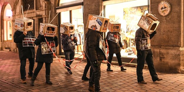 Menschen demonstrieren und tragen Pappkartons auf dem Kopf, die aussehen wie altmodische Fernseher