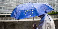 Ein Mensch geht zu Fuß vor der Europäischen Kommission entlang und trägt einen Regenschirm mit dem Symbol der Europäischen Union