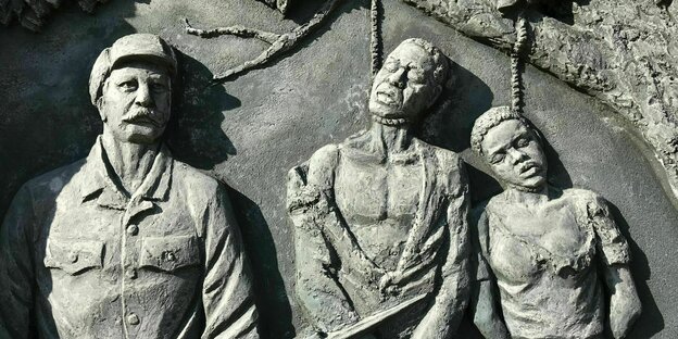 Ein Denkmal, das in Stein gehauene Figuren zeigt. Einen bewaffneten Soldaten und einen Mann und eine Frau, die mit einem Strick gehängt wurden