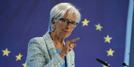 Christine Lagarde steht vor einem Rednerpult und zeigt mit dem Zeigefinger in die Luft
