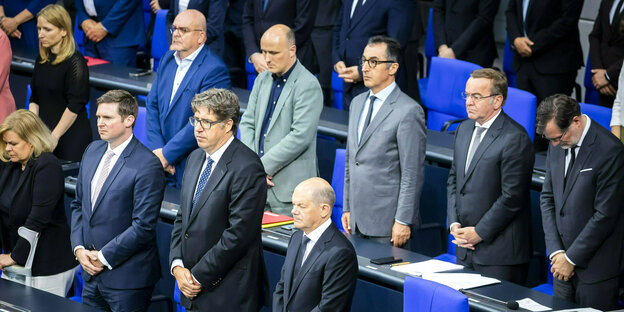 Regierungsmitglieder stehen mit ernsten Gesichtern in der Regierungsbank imPlenarsaal des Bundestages