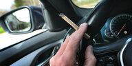 Ein Mann sitzt mit einem Joint zwischen den Fingern am Steuer eines Autos