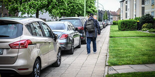 Eine Person läuft einen zugeparkten Gehweg entlang.