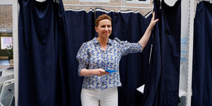 Mette Frederiksen tritt aus einer Wahlkabine hervor. Sie hat die rechte Hand am Kabinenvorhang,den sie zurückgezogen hat