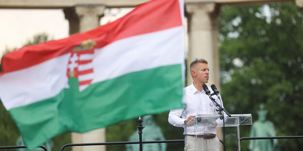 Mann hinter Mikrofon daneben eine ungarische Fahne