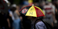 Mensch mit Regenschirm in Deutschlandfarben, auf dem ein durchgestrichenes Hakenkreuz klebt