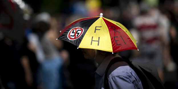 Person mit Regenschirm in Deutschlandfarben, auf dem ein durchgestrichenes Hakenkreuz klebt