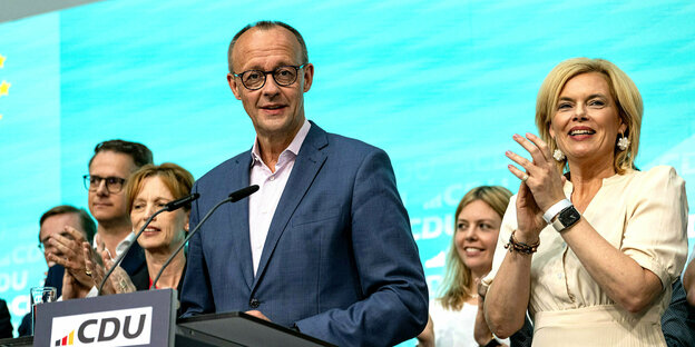 Friedrich Merz am Wahlabend vor einem Rednerpult, umringt von applaudierenden ParteifreundInnen, er wirkt sehr zufrieden