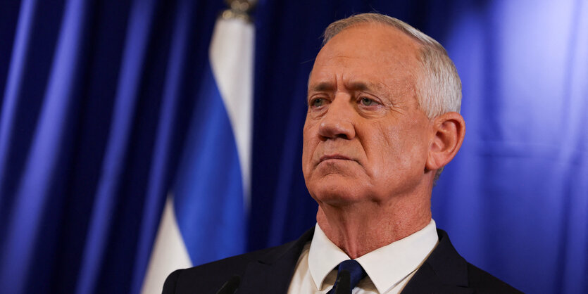 Benny Gantz steht vor einem blauen Hintergrund und schaut grimmig