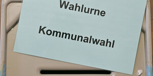 Ein Zettel mit der Aufschrift «Wahlurne Kommunalwahl» liegt auf einer Wahlurne in einem Wahllokal.