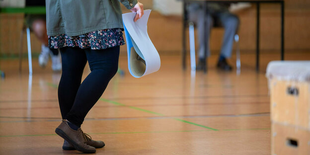 Eine wahlberechtigte Frau wartet in einem Wahllokal mit ihren Stimmzetteln in der Hand auf die Stimmabgabe