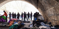 Schlafsäche und Habseligkeiten unter einer Brücke, im Hintergrund mehrere Polizisten