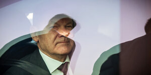 Bundeskanzler Olaf Scholz hinter einer spiegelnden Scheibe seiner Limousine