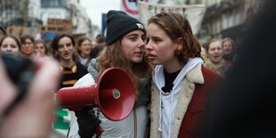 Zwei junge Frauen tuscheln miteinander, eine hält ein Megafon in den Händen