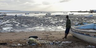 Ein Mann lehnt sich an ein Fischerboot und blickt auf das Meer