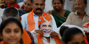 Eine Menschenmenge, einer trägt eine Maske des indischen Premierministers Modi