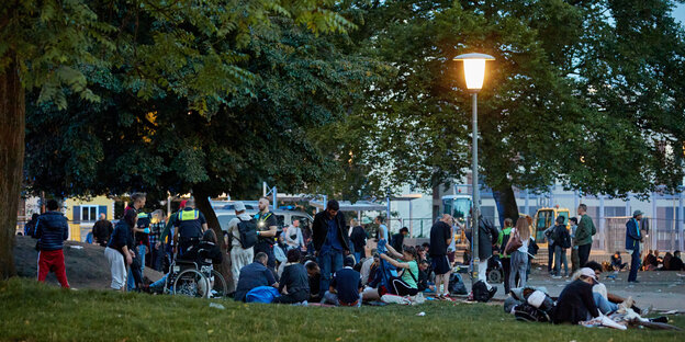 Menschen sitzen in einem Park auf dem Rasen unter einer Laterne