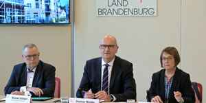 Das Foto zeigt die drei führenden Köpfe der rot-schwarz-grünen Regierunge in Brandenburg bei ihrer Bilanzpressekonferenz: Michael (Stübgen( CDU), Dietmar Woidke (SPD) und Ursula Nonnemacher (Grüne)