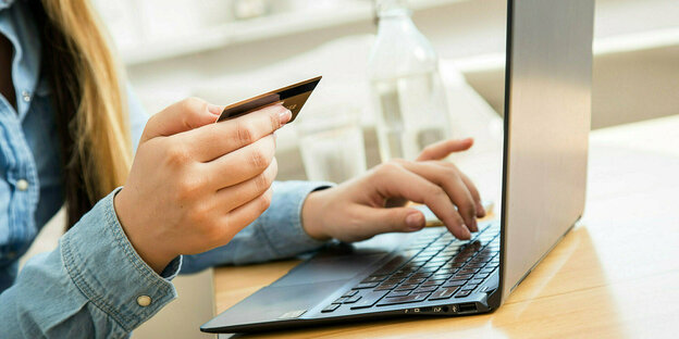 ine Frau sitzt mit einer Kreditkarte am Laptop.