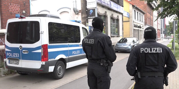 Zwei vermummte Polizisten und ein Polizeitransporter stehen an einer Straße im Norden Braunschweigs. Hier werden die Räume der Deutschsprachigen Muslimischen Gemeinschaft durchsucht.