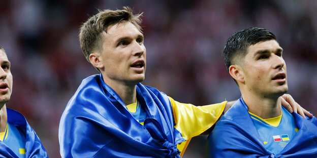 Zwei ukrainische Spieler beim Absingen der Hymne vor dem Spiel mit Fahne um die Schultern.